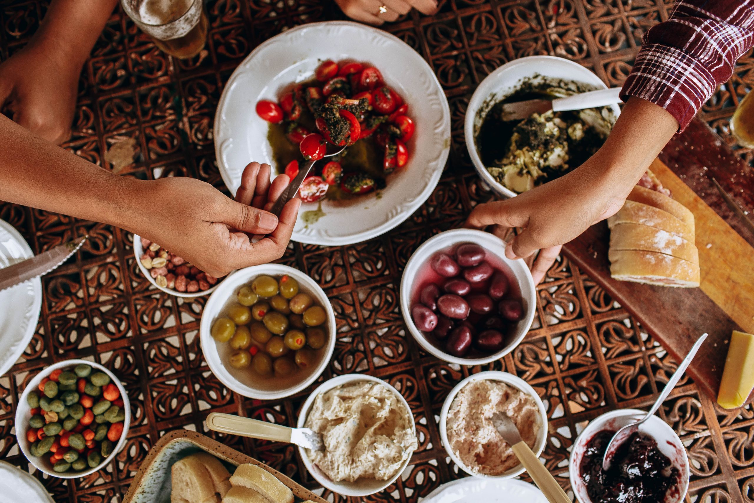 A lively Mediterranean meal with various dishes, showcasing hands reaching for olives and bread.